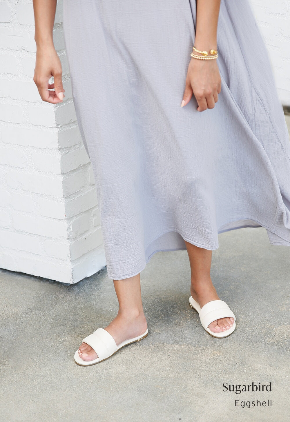 Woman wearing Sugarbird leather slide sandals in eggshell with gray dress