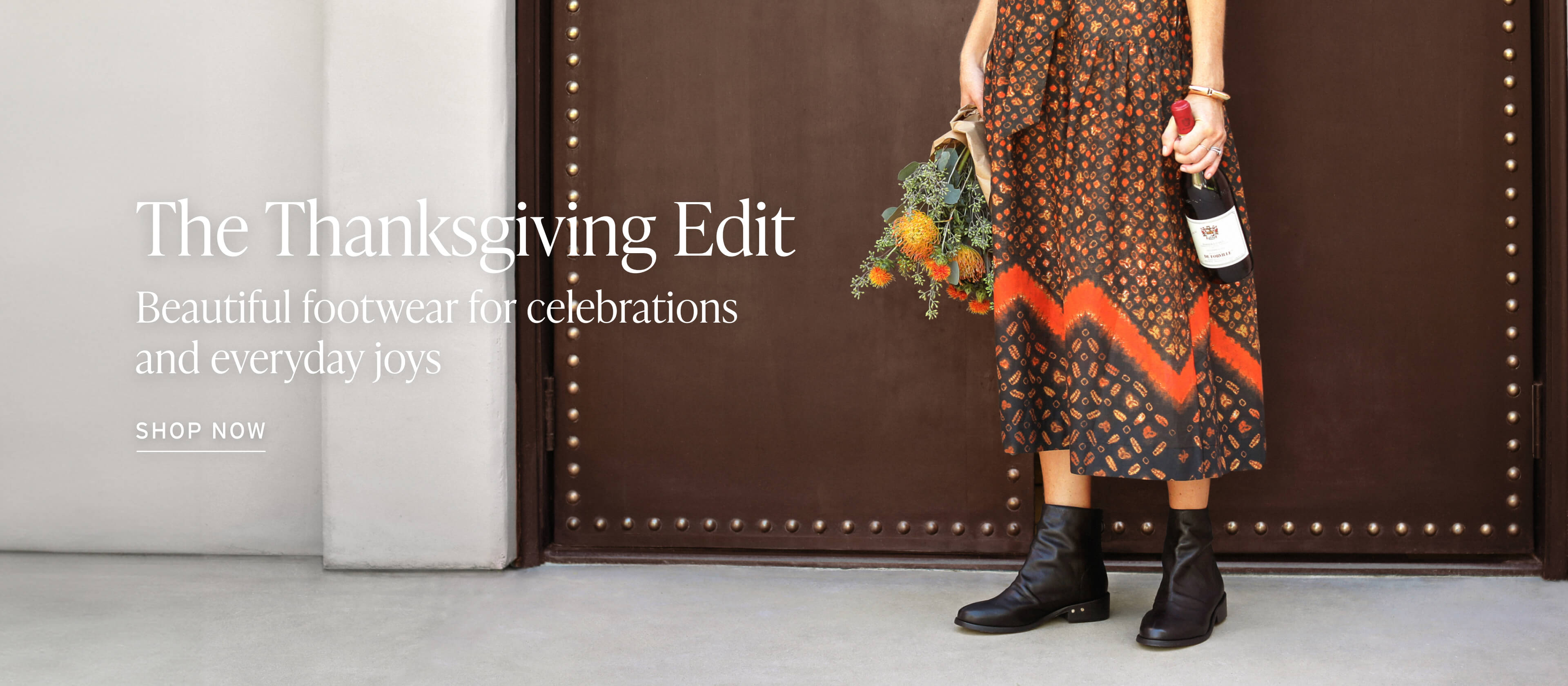 Woman wearing Hawk leather boots in blsck with. floral dress holding flowers and wine. Header: The Thanksgiving Edit. Bzeautiful footwear for celebrations and everyday joys. Shop Now.
