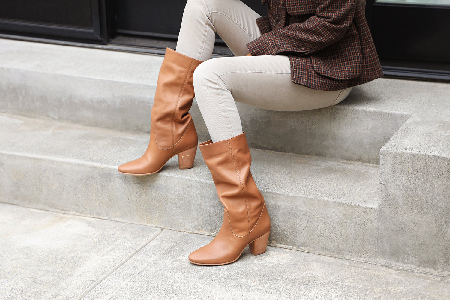 Woman wearing Crow tall leather boots in tan with beige pants and c jacketplaid