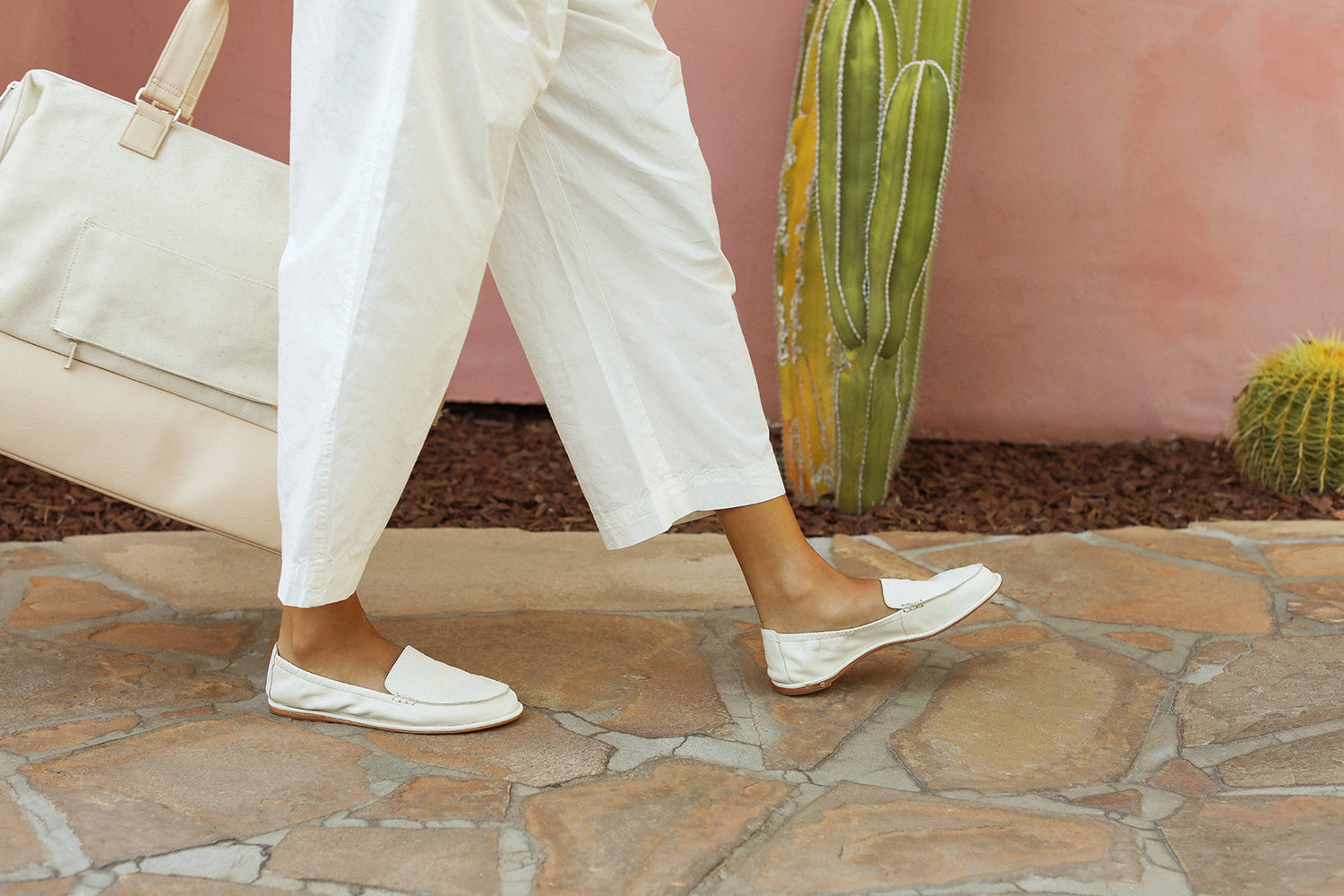Woman wearing Griffin leather loafers in vanilla with white pants holding travel bag