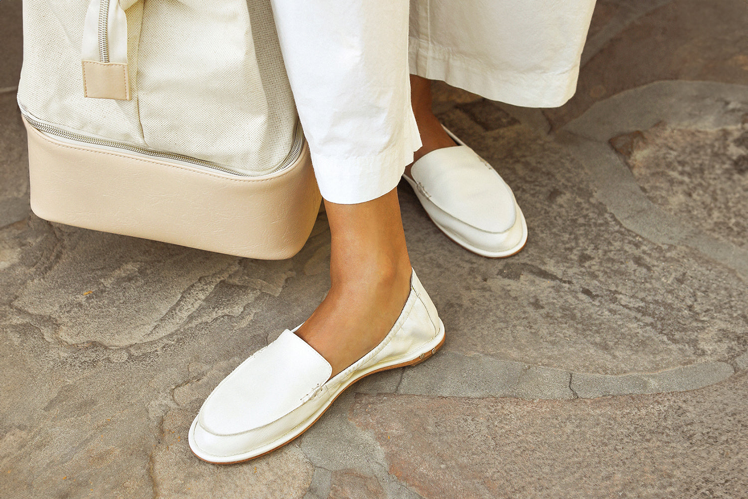 Woman wearing Griffin leather loafers in vanilla with white pants holding travel bag