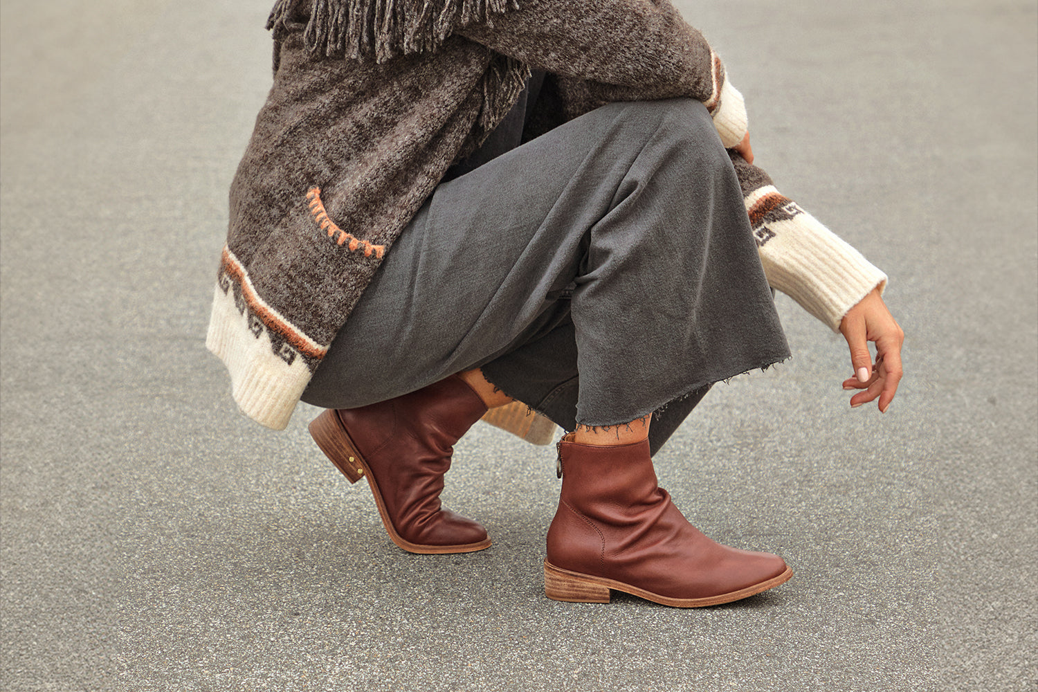 Woman wearing Hawk leather ankle boot in mahogany with gray pants and fringed sweater