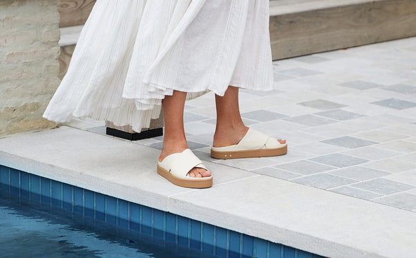Woman wearing Hen leather platform criss-cross sandals in eggshell with white dress