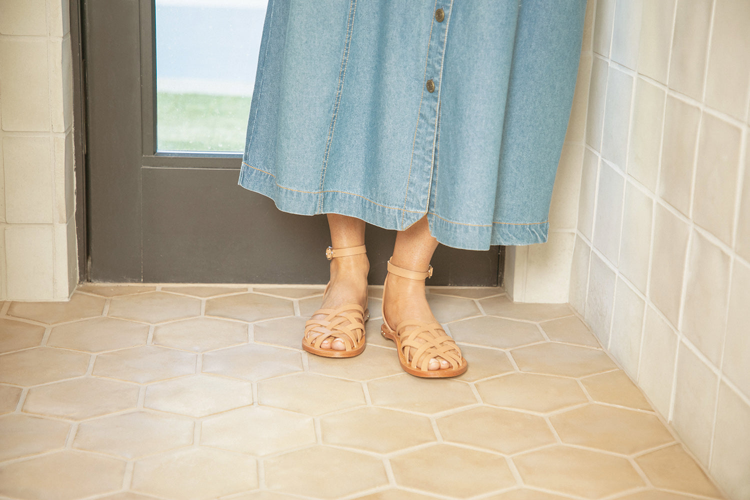 Woman wearing Merlin leather ankle strap sandals in honey with denim dress