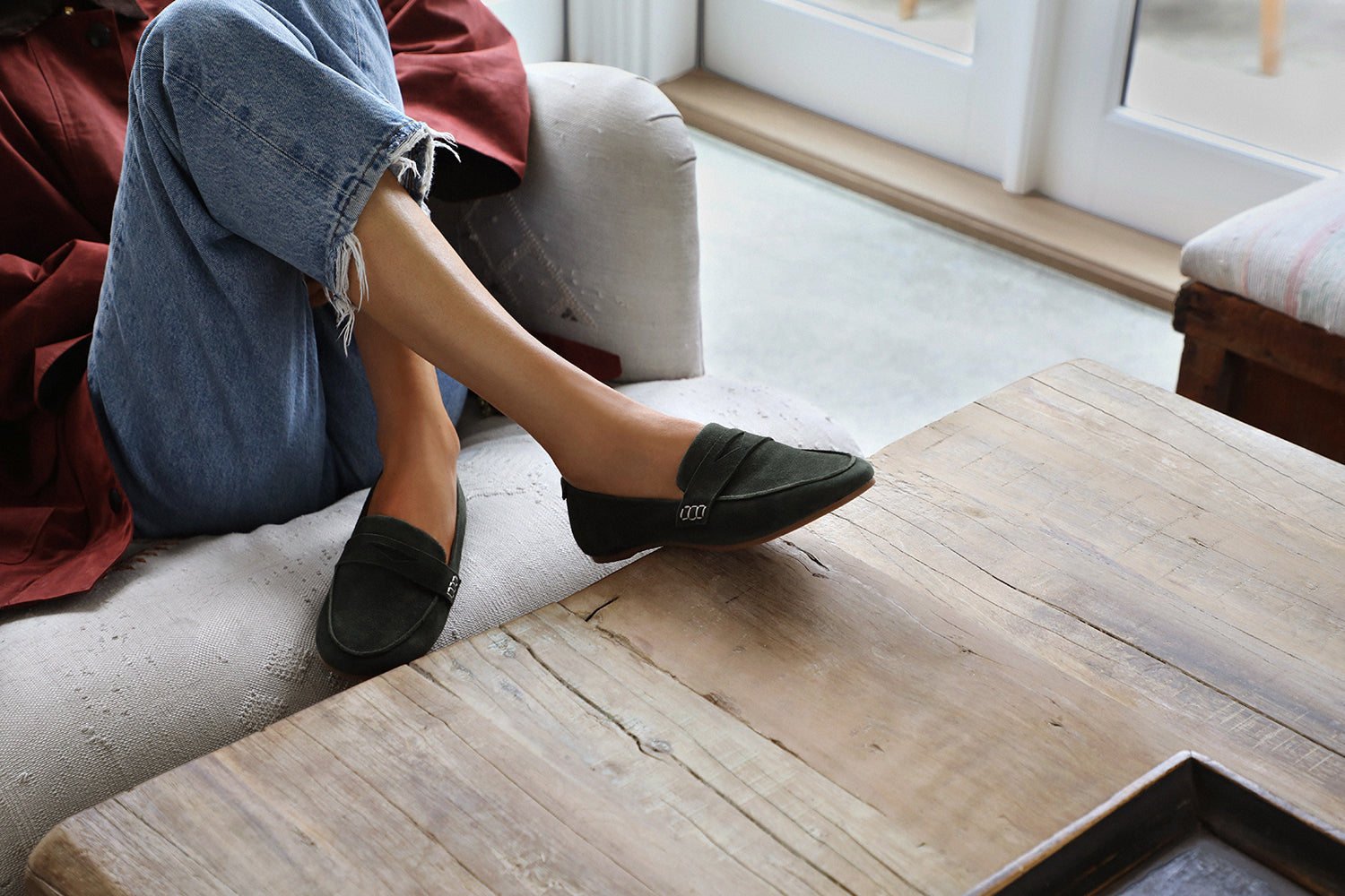 Woman wearing Moorhen suede loafers in ivy with jeans on couch