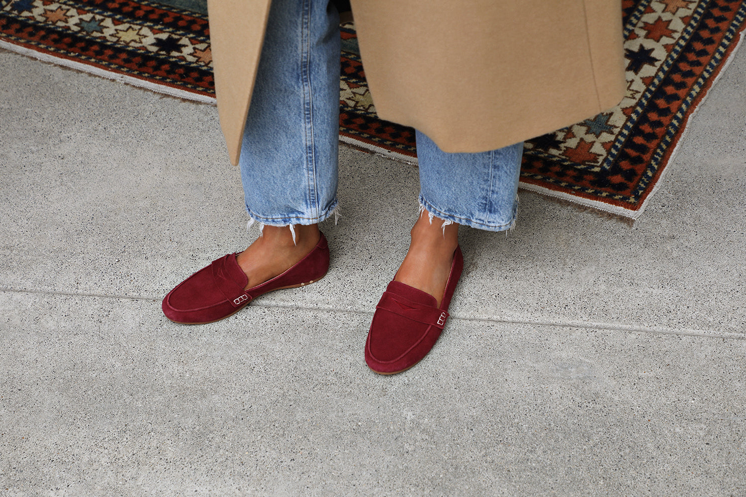 Woman wearing Moorhen suede loafers in port with jeans and long coat.