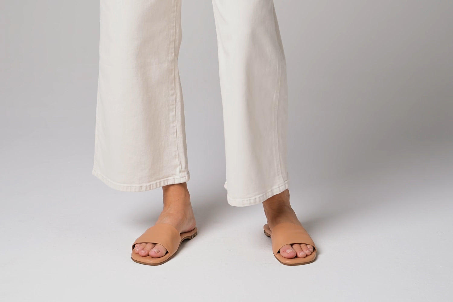 Video of woman walking in Honeybird leather slide sandals in beach with white pants.