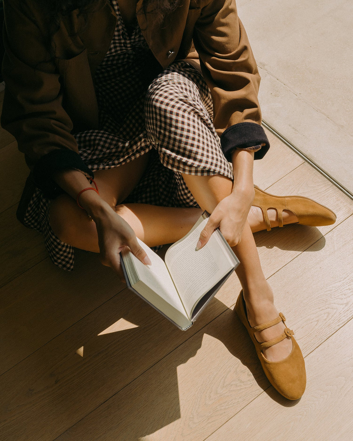 Woman wearing Partridge leather mary jane ballet flats in toffee with checkered dress, reading a book