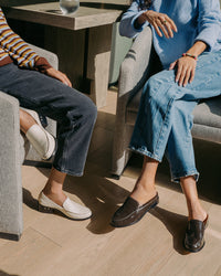Women sitting, wearing Owl leather loafer in eggshell and Owlet patent leather loafer mule in coffee with jeans.