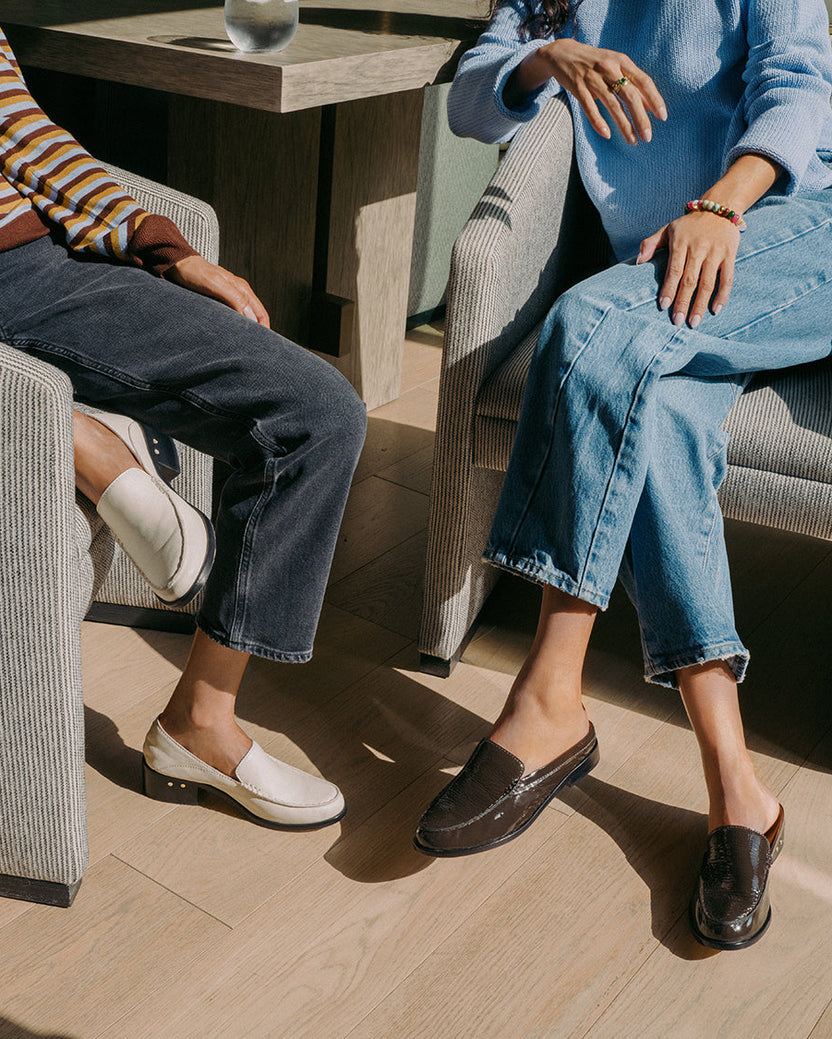 Women sitting, wearing Owl leather loafer in eggshell and Owlet patent leather loafer mule in coffee with jeans.