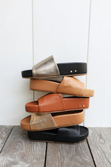 Group shot of Pelican leather slide sandals in bronze/black, honey, tan, gold/honey, and black colors.