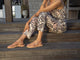 Woman wearing Auklet leather strappy toe-ring sandal in beach with patterned jumpsuit