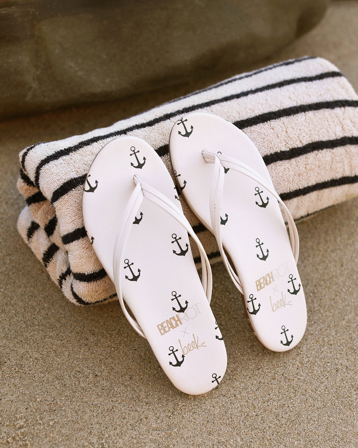 Beachbird leather flip flop sandals in vanilla/navy propped on beach towel