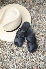 Bittern woven leather sandals in black next to hat