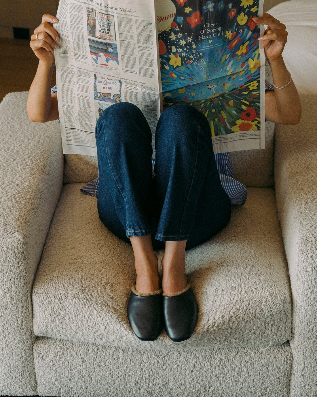 Woman wearing Blackbird Shearling leather mules in black with jeans holding up newspaper