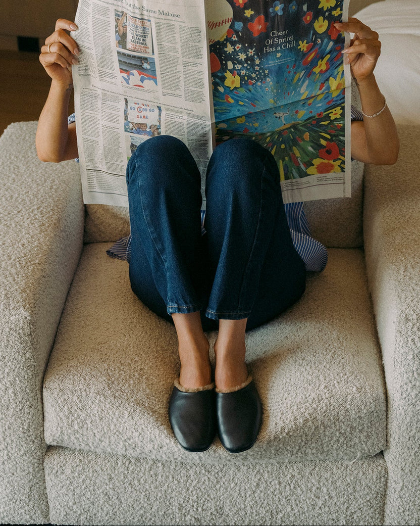 Woman wearing Blackbird Shearling leather mules in black with jeans holding up newspaper