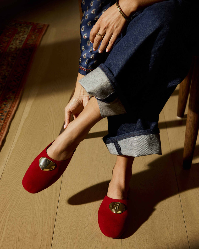 Woman wearing Blackbird Bling suede mule in crimson with attached gold charm with cuffed jeans and paisley blouse