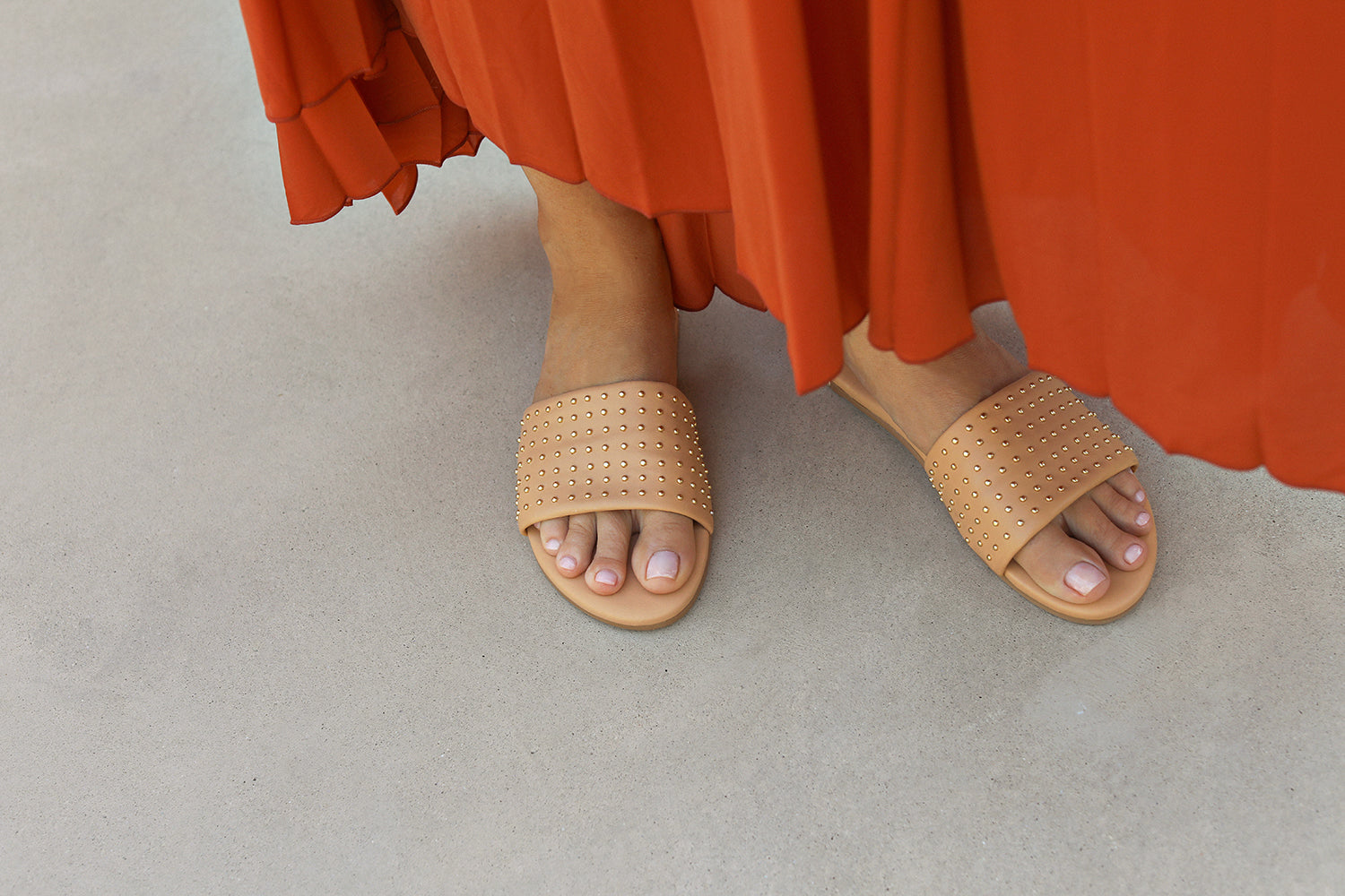 Woman wearing Blingbird leather studded slide sandals in beach with orange dress