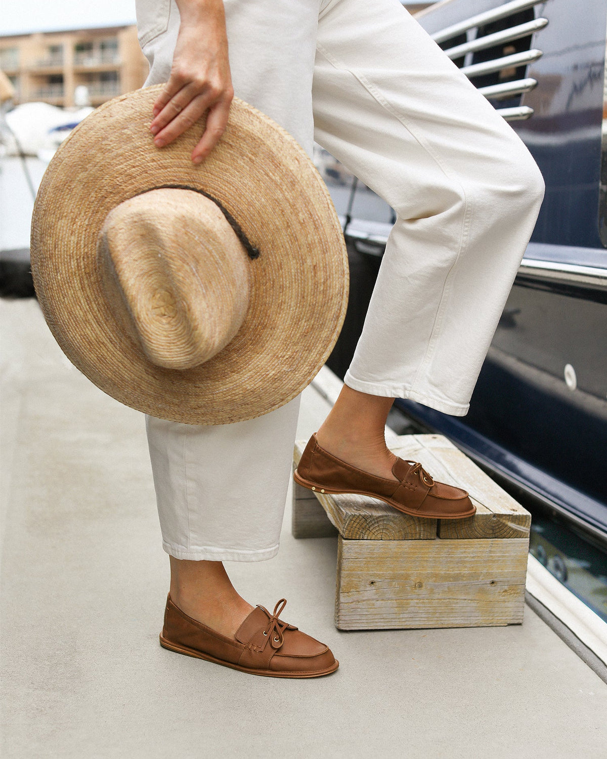 Woman wearing Boatbird leather loafers in cognac with white pants and sweater by a boat