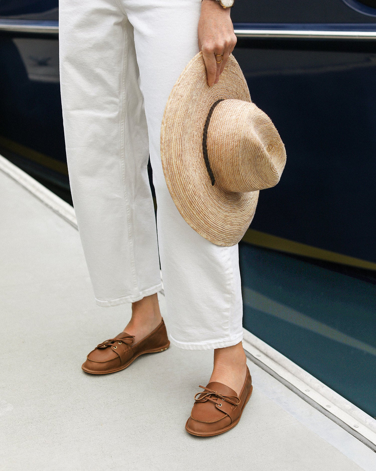 Woman wearing Boatbird leather loafers in cognac with white pants and sweater by a boat