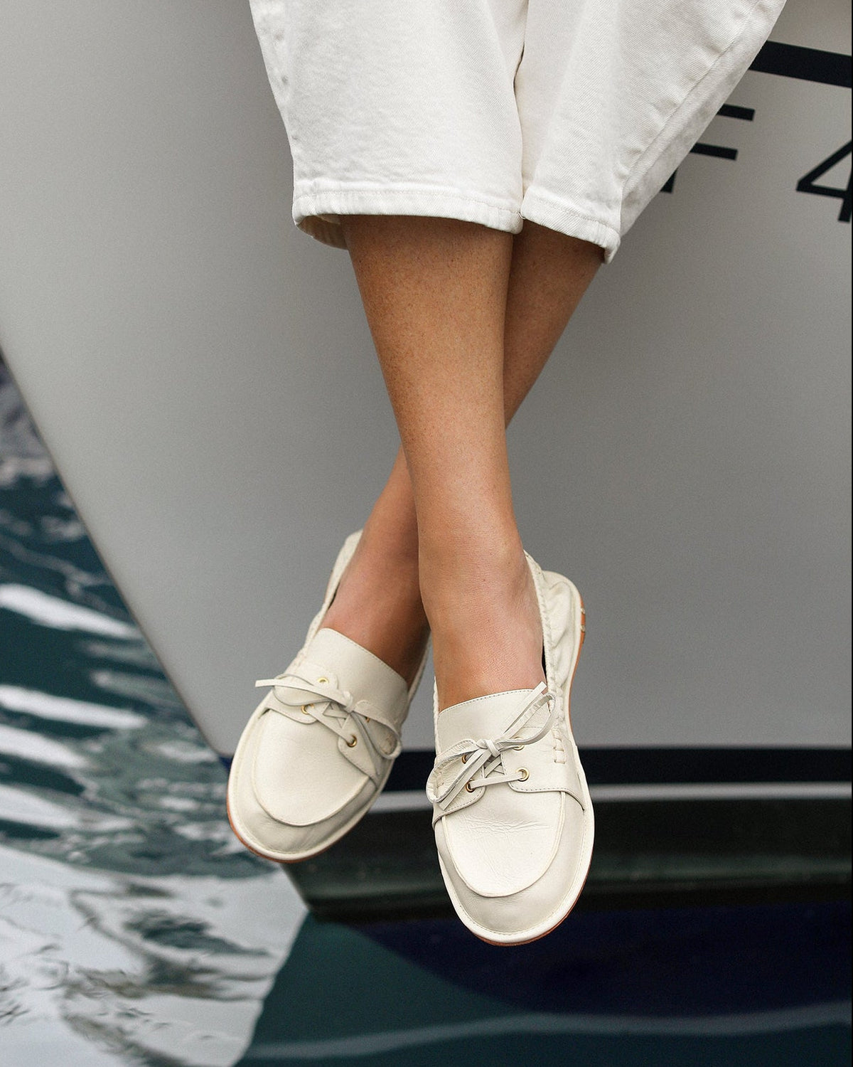 Woman wearing Boatbird leather loafers in vanilla with white pants and sweater on a boat