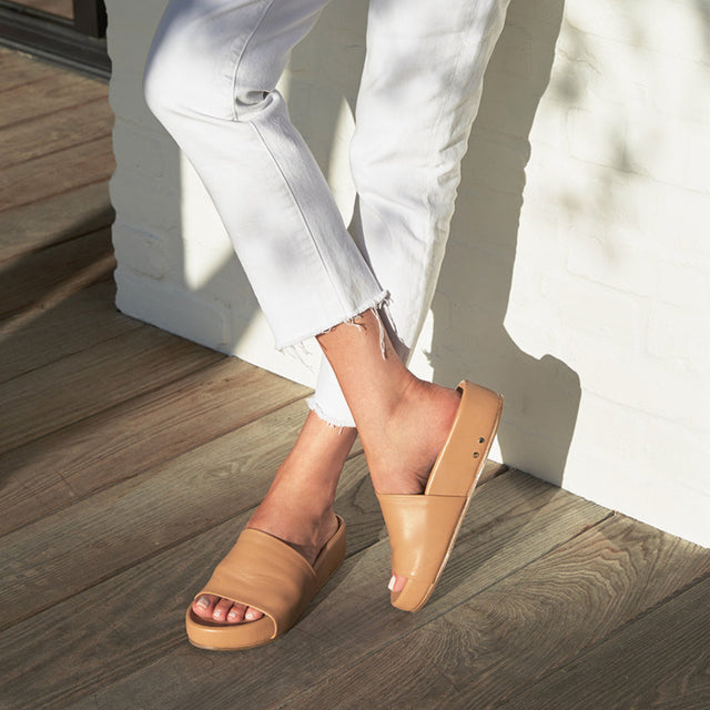 Woman wearing Pelican leather slide sandal in honey with white jeans