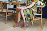 Woman wearing Condor leather boots in cognac with green dress, holding wine glass.