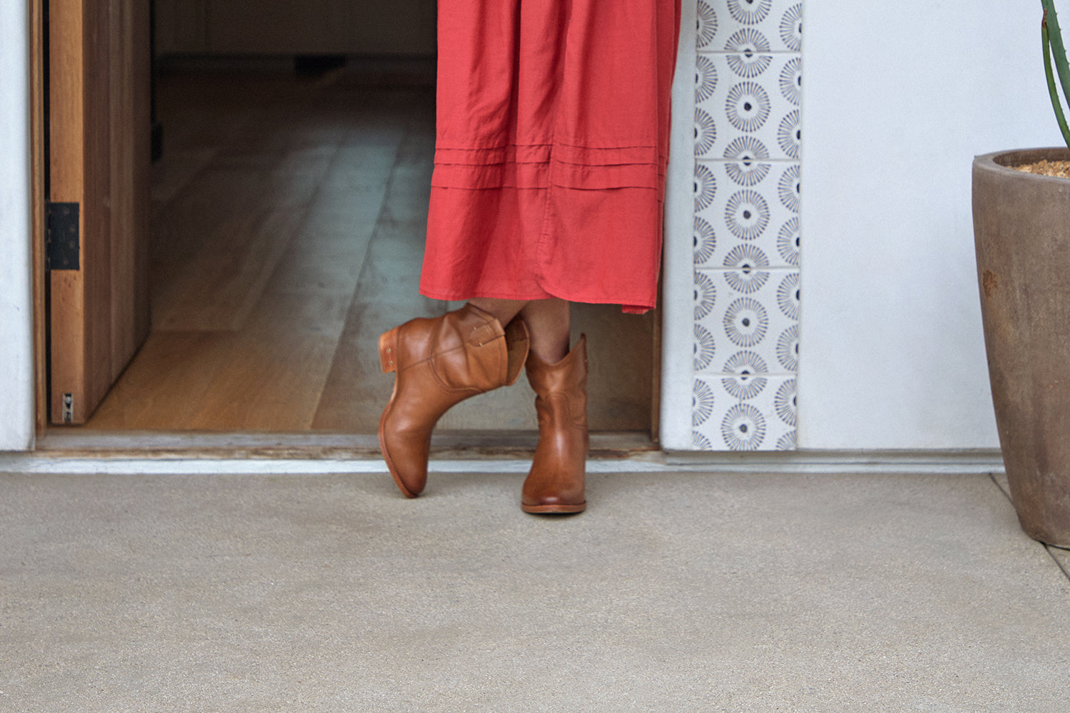 Woman wearing Condor leather boots in tan with red dress standing in doorway