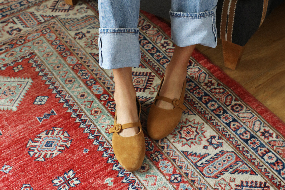 Woman wearing Crane suede mary jane shoe in caramel with jeans on rug
