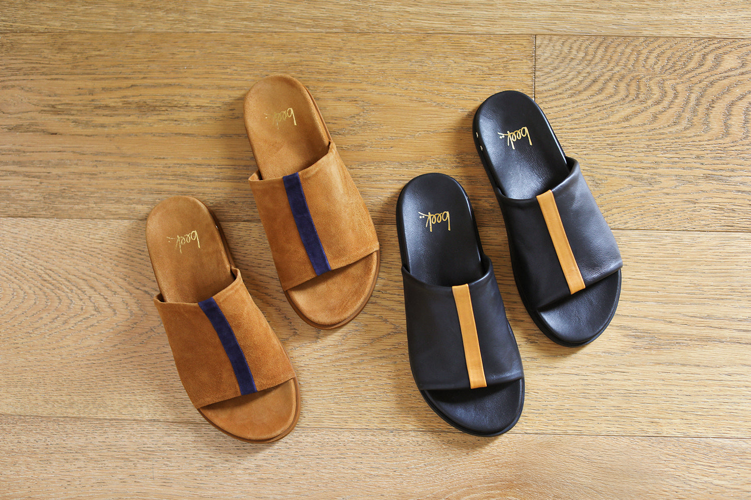 Group shot of Crest suede slide sandals in caramel with navy stripe with Crest leather slide sandals in black with tan stripe.