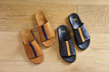 Group shot of Crest suede slide sandals in caramel with navy stripe with Crest leather slide sandals in black with tan stripe.