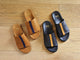 Group shot of Crest suede slide sandals in caramel with navy stripe with Crest leather slide sandals in black with tan stripe.