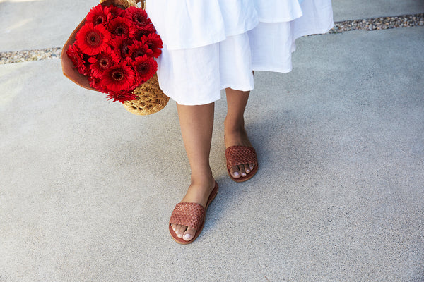 Woman wearing Fairy woven leather sandals in tan with white dress, holding flowers