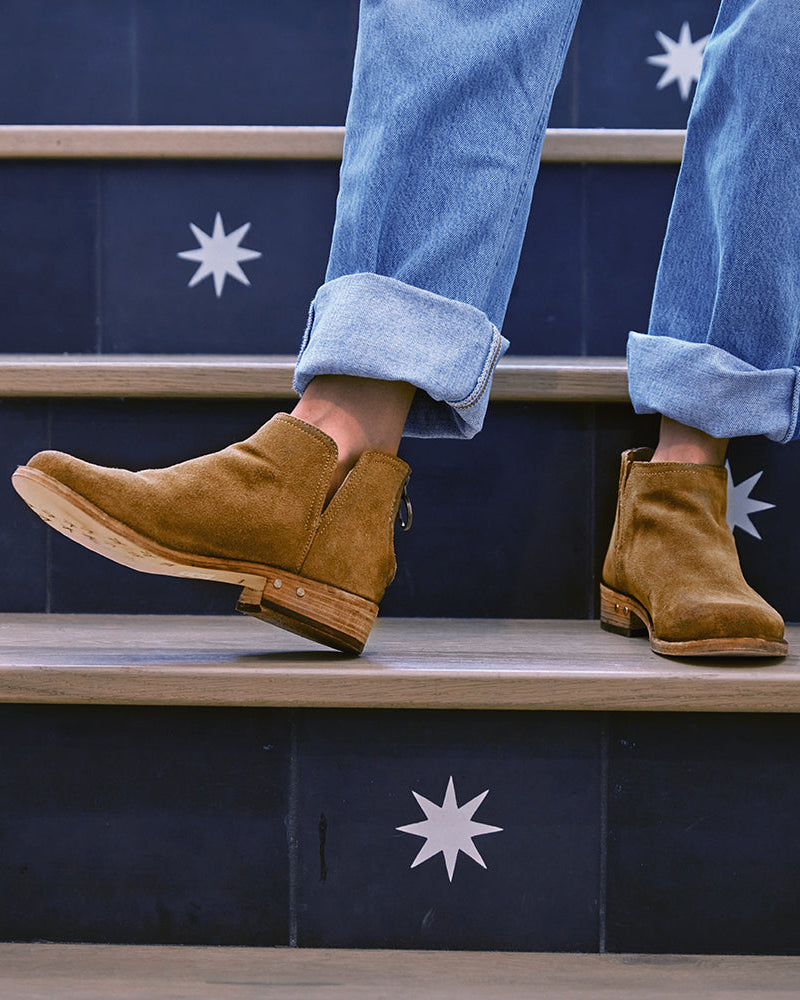 Woman wearing Falcon suede booties in chestnut with jeans on steps
