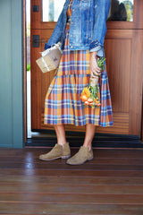 Woman wearing Falcon suede booties in chestnut with plaid dress and jean jacket, holding package and flowers.