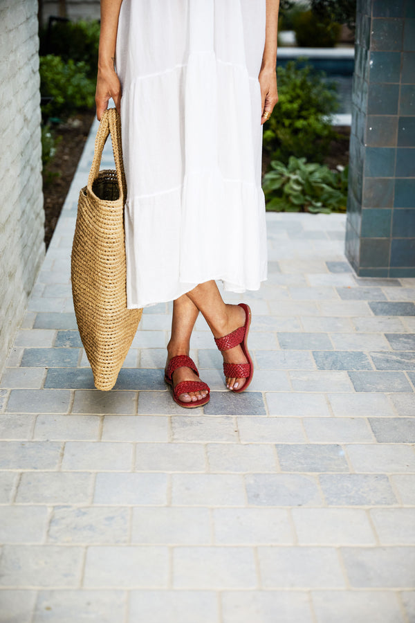 Woman wearing Flicker woven leather sandals in red with white dress and woven tote.