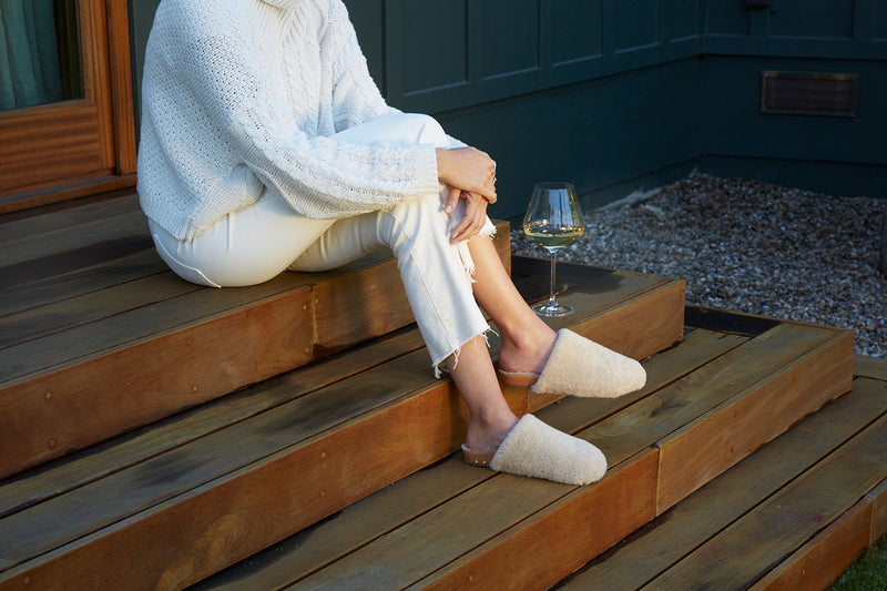 Woman wearing Flufftail shearling mule in natural/honey with white pants and sweater.
