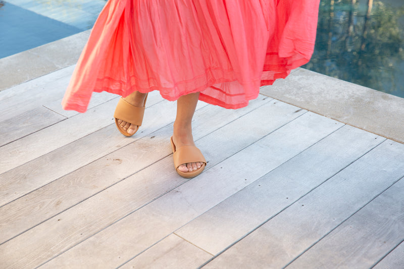 Woman wearing Gallito leather slide sandals in honey with coral dress.