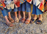 Women wearing Gallito Shearling suede slide sandal in Pecan, Gallito Más Shearling suede slide sandal in almond, Gallito Más Shearling leather slide sandal in cognac, Gallito Shearling leather slide sandal in black with jeans, carrying a blanket.