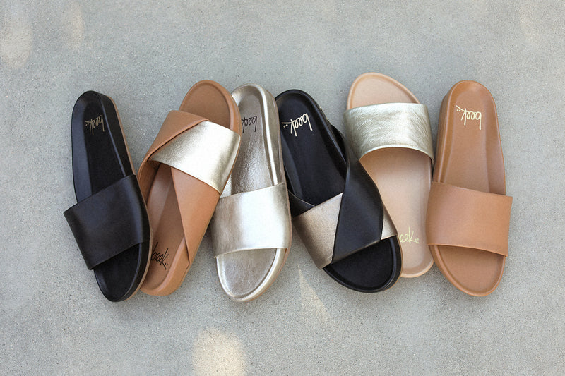 Group shot of Gallito leather slide sandals in black, platinum, platinum/beach, honey with Paloma leather slide sandals in gold/honey and bronze/black.