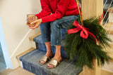 Woman wearing Gallito Shearling leather slide sandals in bronze with jeans and red sweater by holiday garland.