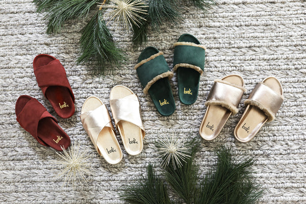 Group shot of Kea slides in wine suede and gold leather colors next to Gallito Shearling slides in forest suede and bronze leather. 