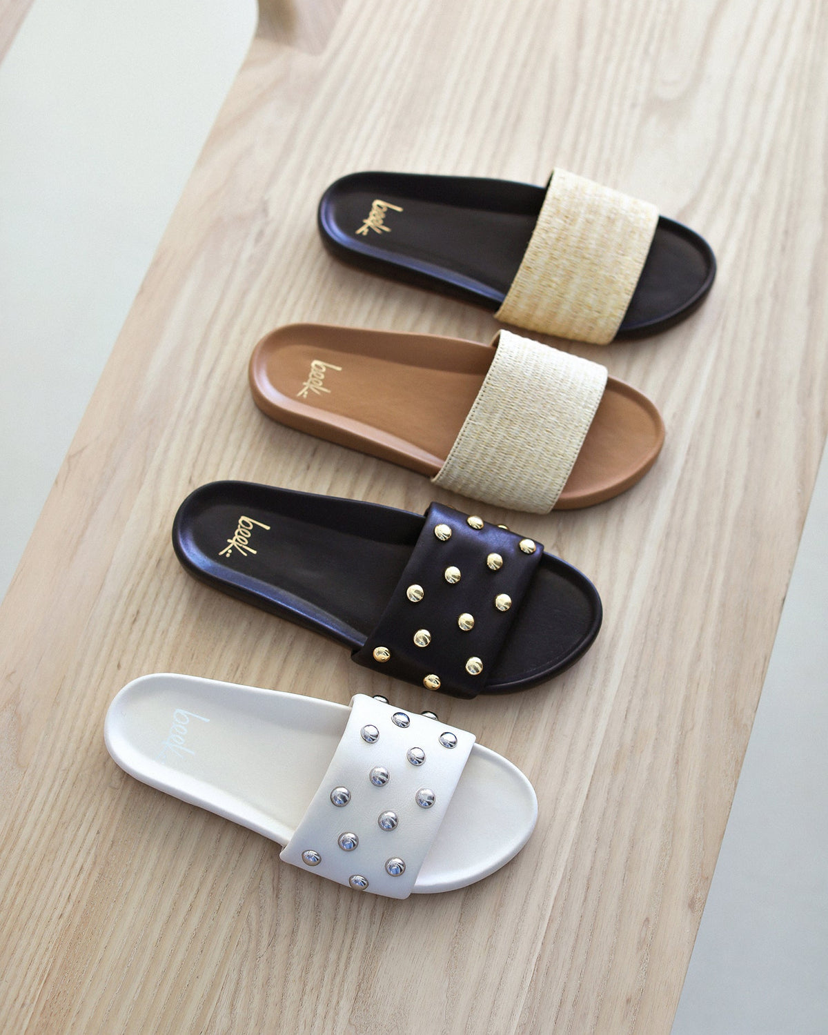 Group shot of Gallito Raffia leather slide sandals in honey and black and Gallito Stud leather slide sandals in vanilla and black.