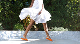 Woman wearing Gallito leather slide sandals in tangelo with white dress