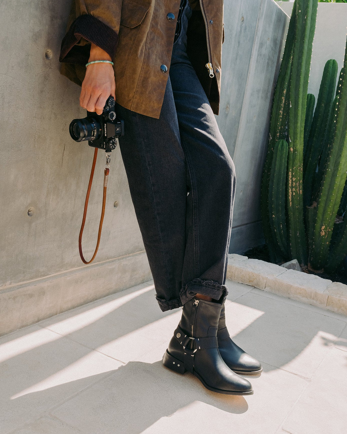 Woman wearing Grackle leather boots in black with dark jeans and coat, holding camera
