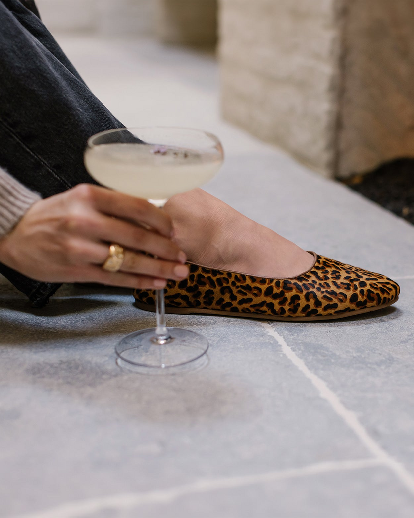 Woman wearing Swiftlet calf hair ballet slippers in leopard holding cocktail