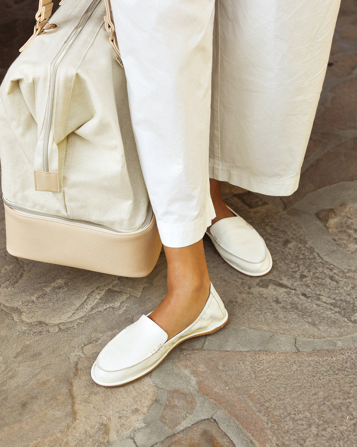 Woman wearing Griffin leather loafers in vanilla with white pants carrying a travel bag