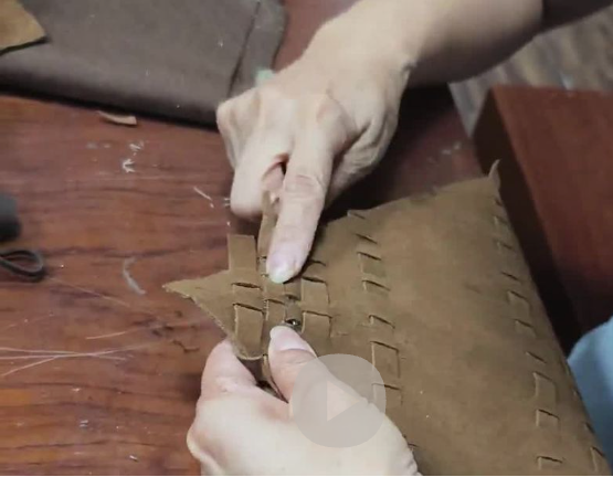 A close-up of a person's hands weaving a brown leather strap into a woven leather case on a wooden workbench.