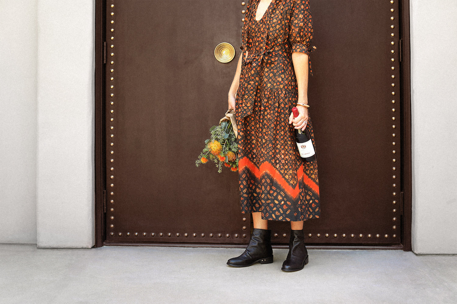 Woman wearing Hawk leather boots in black with patterned dress holding flowers and wine