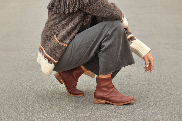 Woman wearing Hawk leather ankle boot in mahogany with gray pants and fringed sweater